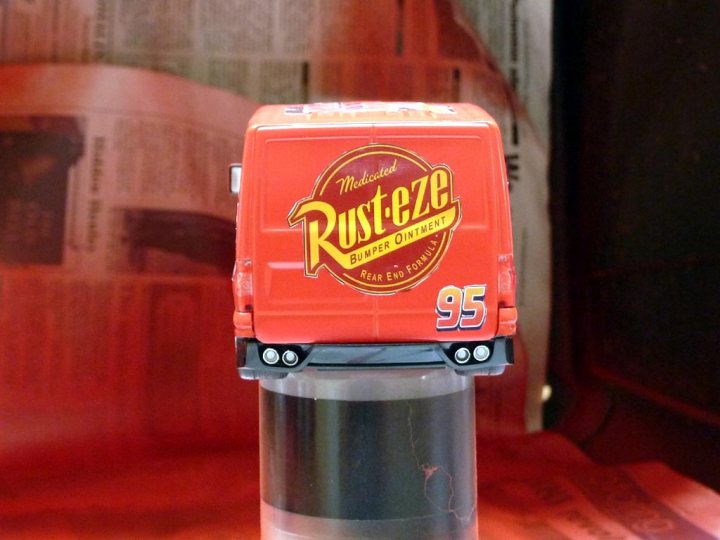 Challenge Pistonheads Scalextric Van Transit - The image features a small, toy-sized replica of a Rust-Eze Tire Rotator, which is predominantly red with text indicating it as "RUST-EZE," "NATURAL LUBRICANT," "JOHNSON & JOHNSON," and "95." The toy is made from plastic and includes wheels and four posting prongs for standing upright. It's positioned against a background with text and images that appear to be unrelated to Rust-Eze or the toy. The toy seems to be a piece of memorabilia or collectible item for enthusiasts of vintage or promotional kitchen appliances.