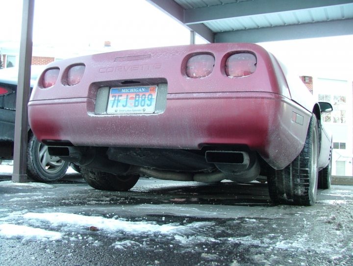 Snow Pistonheads Driving - The image shows a vibrant red Chevrolet Corvette car parked in a garage. The car's license plate reads "TJ 889". The vehicle appears to be covered in a layer of ice or frost, suggesting that the weather is cold. The Chevrolet Corvette is a sleek and powerful sports car, known for its distinctive shape and performance. The tires of the car are visible, and the reflection on the ground indicates that the photo was taken from a slightly elevated position.