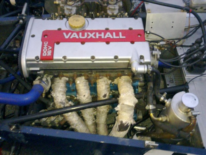 Rebuild Pistonheads Caterham Winter - The image depicts the internal view of a vintage car's engine. The most prominent feature is the silver engine block labeled "Vauxhall," suggesting a vintage British vehicle. The bracket of the car's radiator is also visible in the image, painted in a shade of blue. A close-up view reveals several hoses and the car's rusty piping beneath a somewhat gristly appearance. The overall scene portrays the complexity and mechanical beauty typical of classic automotive designs.