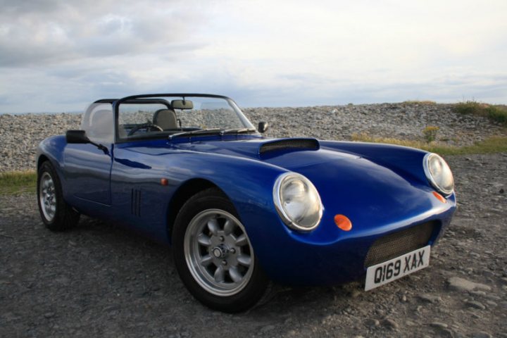 A classic car is parked on the grass - Pistonheads - The image showcases a blue sports car with a distinctive design and classic aesthetic. The car is positioned in the center of the frame, its glossy surface reflecting part of the rocky ground it's parked on, possibly an abandoned dirt road. The car radiates a sense of motion and adventure. Its license plate is clearly visible, providing a touch of realism. The distant view of a rocky outcrop provides a stark contrast to the smooth curves of the car, suggesting isolation and a sense of calmness that often accompanies such locations.