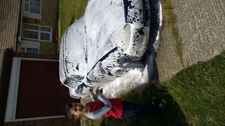 A dog wearing a hat and a hat - Pistonheads - The image depicts a child standing on a driveway in front of a car that has been sprayed with a black and white substance. The child, dressed in a red shirt and brown pants, appears to be looking at the car with interest. The fondant substance covering the car contrasts with the bright color of the child's shirt. The driveway leads to a garage, which is partially visible in the background. The surroundings suggest a residential area, possibly in a community located on the outskirts of a city.