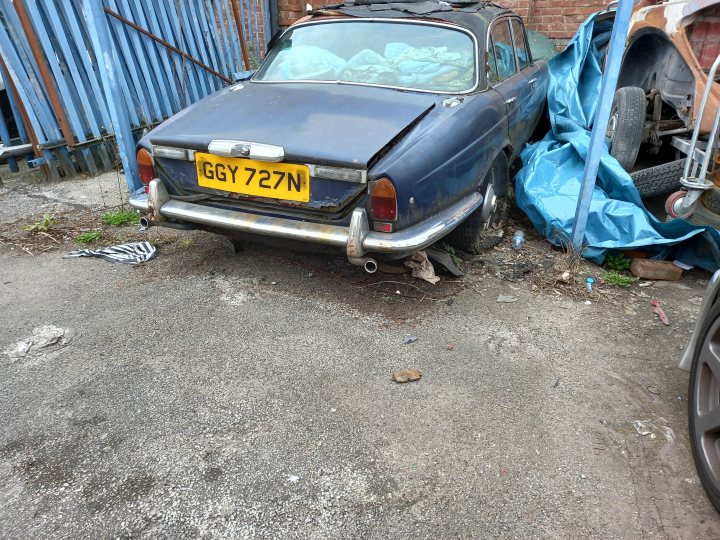 Classics left to die/rotting pics - Vol 2 - Page 340 - Classic Cars and Yesterday's Heroes - PistonHeads UK - The image shows a dilapidated classic car that appears to be in a state of disrepair. It is parked in a lot with other vehicles and has an open hood, suggesting it may have been taken apart for repair or restoration. The vehicle's bodywork is rusted and damaged, indicating it has been exposed to the elements for some time. In the background, there is a building with a metal fence, partially obscured by the car. There are also various items scattered around, including a piece of cloth draped over a part of the car. The license plate of the car reads "Y71 NJ". The overall impression is one of abandonment and neglect.