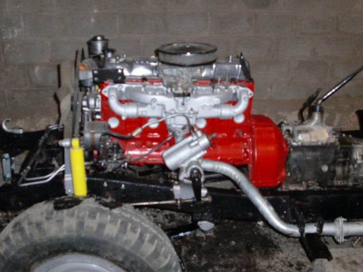 Toyota FJ40 - Page 1 - Off Road - PistonHeads - The image shows a partially disassembled red and white motor, which appears to be missing some parts and might be under repair or modification. The engine of the motor, which has a manual transmission, is partially exposed, revealing its red and white parts. In the background, there's a concrete wall which seems to be an old building. The focus of the image is on the motor's engine and transmission area, which are prominently in the foreground.