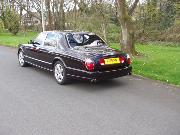 A car is parked on the side of the road - Pistonheads - The image shows a dark-colored four-door car parked on the side of a road. The car is shiny, suggesting that it might not be raining. The interior light of the car is on, and it is located near a gazebo and a grassy area in a park-like setting.