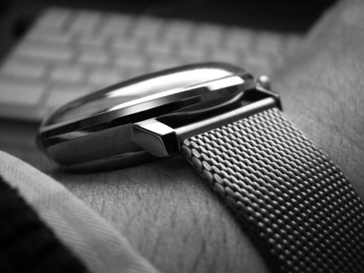 Wrist Pistonheads Check - The image captures a moment of tranquility. On a table, a silver watch with a mesh band is the main focus. The watch is positioned in such a way that it rests on the edge of a table, with the keyboard in the background. The hands of the watch, marked with black hours, indicate the time. The color palette of the image is monochrome, adding to the calm and serious atmosphere.