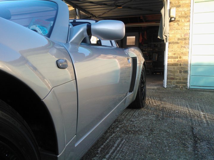 Pistonheads - The image shows a gray sports car parked in a garage with a silver mirror and emblem on the front. The car is sleek and modern, suggesting speed and performance. The garage has a concrete floor and a white door with a window, providing a clean and well-maintained background for the vehicle. The lighting in the scene indicates that it's daytime. The car is positioned in such a way that it dominates the frame, drawing attention to its design and detail.