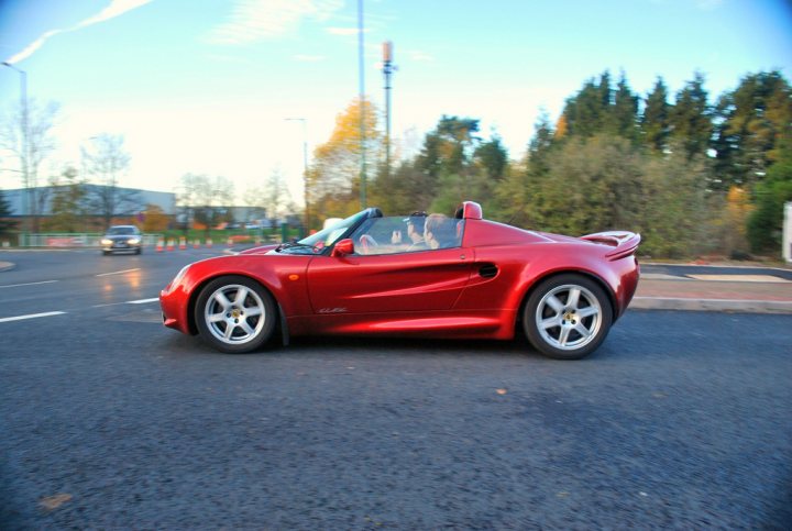 Required Passengers Mph Pistonheads Drivers - The image captures a vibrant scene on a road. A red sports car is the main focus, parked near the center of the image. It's a captivating vehicle with its sleek design and aggressive performance stance suggested by its large aftermarket spoiler. The car is parked on a paved surface, with a background of trees providing a natural setting. There are other elements in the scene as well, such as a pedestrian and a car in the distance, adding to the everyday dynamism of the image.