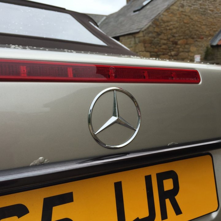 Mercedes 129 titivation - Page 1 - Readers' Cars - PistonHeads - This is a close-up image of the rear view of a silver Mercedes-Benz car. The rear light is red in color with the logo prominently displayed. The background is out of focus, but it appears to be a clear day with the top of a building in the distance. The license plate is shown, but it is not appropriate to interpret or provide information related to the registration. The car's rear bumper is visible with no damage or debris. The image captures the elegance and attention to detail that is characteristic of Mercedes-Benz vehicles.