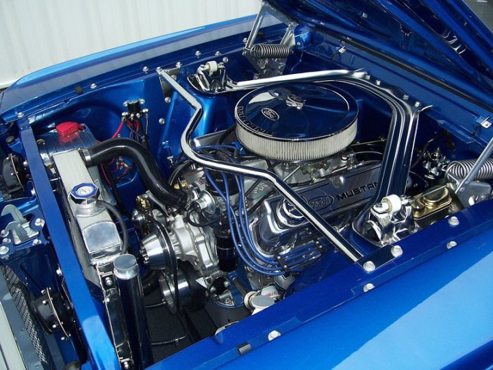 New owner what do you guys think. - Page 1 - Mustangs - PistonHeads - The image shows the engine bay of a blue car, featuring a prominent engine with an unusual collage design on its cover. The engine compartment is open, revealing the inner workings, hoses, and various mechanical components. The text "MUSTANG" is visible on the engine cover, suggesting branding and indicating the model of the car. The engine appears modern and powerfully, implying that this vehicle is a high-performance Mustang.