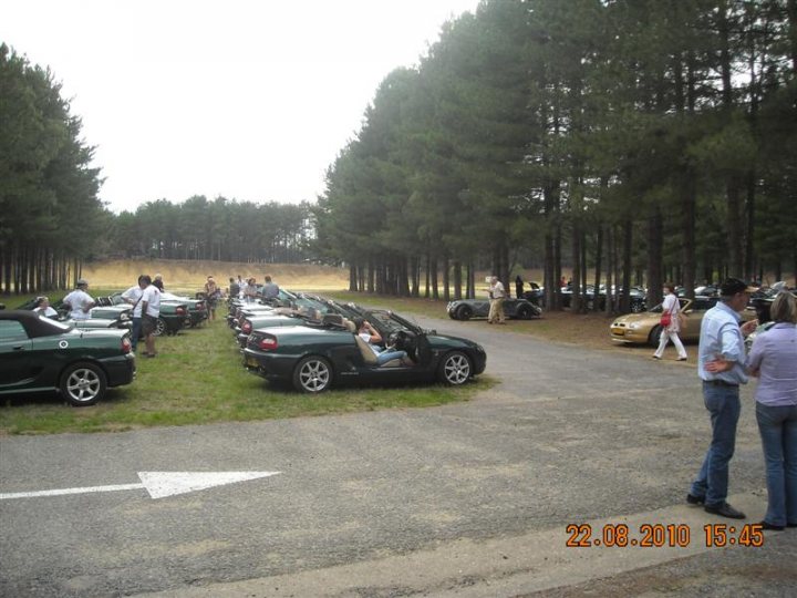 Pistonheads - The image depicts a parking lot filled with numerous cars parked neatly in rows, suggesting a well-organized event or gathering. The lot is lined by a mix of trees and lush green grass, with a pathway leading through the center, indicating a clear route for pedestrians. A pedestrian is captured mid-stride, adding dynamism to the scene. The photo is timestamped, indicating it was taken on a clear day on April 8th, 2010, at 15:45. The cars and the person are positioned in the center of the frame, suggesting the focus of the event or the direction of the pathway.