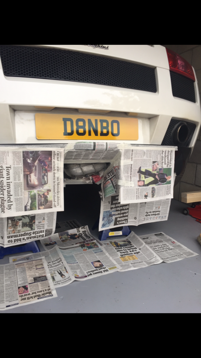 A kitchen with a refrigerator and a stove - Pistonheads - The image shows a close-up of car parts with a litter of newspapers around them. The focus is on the rear section of a white vehicle, where the registration plate is partially visible. The registration plate is painted in black and red to distinguish it from the rest of the car. The car is situated on what appears to be a garage or workshop floor. The scattered newspaper articles suggest a casual, unorganized setting, perhaps a place where tinkering or maintenance of the car is taking place.