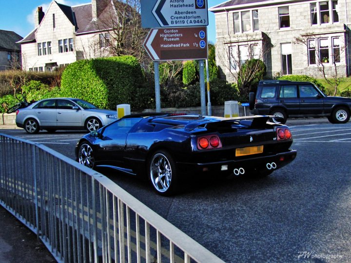 Supercars Spotted Pistonheads Rarities - The image captures a scene of a small, black, two-door sports car parked on a street. The car's sleek design and shiny finish are prominent in the foreground. In the background, there's a residential area with several parked cars that are smaller and more subdued in comparison to the sports car. A sign is visible on a pole, although its details are not clear from this angle. The overall setting suggests a peaceful neighborhood environment with ample space for vehicles.