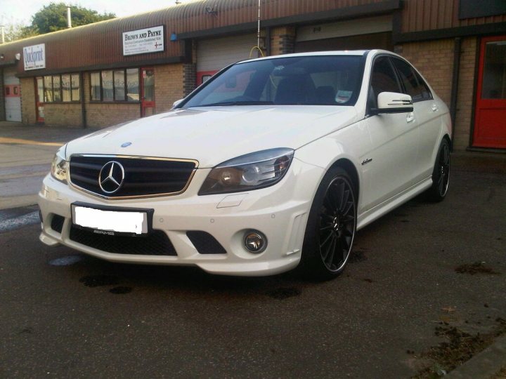 Show us your Mercedes! - Page 9 - Mercedes - PistonHeads - The image shows a car parked in front of a building. The car is predominantly white with black rims and features a sleek design. It appears to be a Mercedes vehicle, as indicated by the grille and crest. The car is parked on a concrete surface that complements the overall clean and tidy appearance of the scene. There is a sign with an arrow in the background, suggesting this might be a parking lot or a similar commercial area.