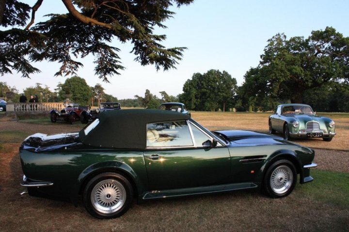 Sale Aston Pistonheads - The image depicts a sunny day at a park, with the main focus on a vintage British roadster parked on grass. The car, painted in a rich green color and adorned with a contrasting black top, is positioned in front of another car, and there are several others in the background. A few people are visible around the cars, some standing by and others just passing by. In the distance, trees can be seen, providing a natural backdrop to this outdoor gathering of cars and people.