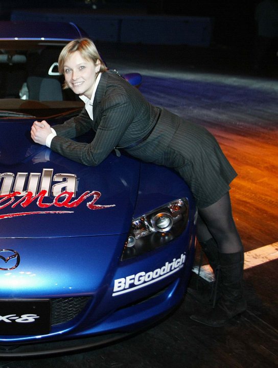 Pistonheads Axed Gear - In the image, a young woman is seen kneeling in front of a striking blue sports car. She is dressed in fashionable attire, her hands placed gently on the gleaming hood of the car. Her posture suggests she is posing for a photo, perhaps indicating her interest in fast cars or luxury items. The car bears the inscription "BFFGOODRICH", suggesting a connection to luxury vehicles and possibly a specific brand or model. The overall atmosphere seems to be indoors, possibly a showroom or car exhibition, under blue lighting that accentuates the blue color of the car.