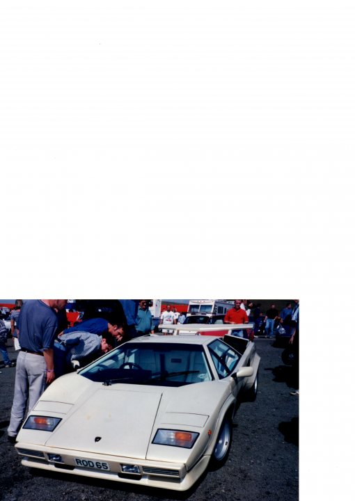 Old-school Supercars - Page 4 - Scotland - PistonHeads - The image features a white car in the foreground parked on a gravel-y covered surface, surrounded by several people. In the background, there is a red vehicle, enhancing the color contrast. The people are scattered around the area, suggesting a casual gathering or event. The image seems to capture a moment at an outdoor event or a parking area adjacent to such a location. The photo has the quality of a standard print, with no obvious signs of digital manipulation.