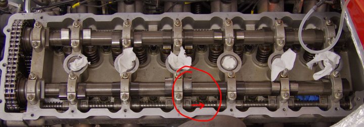 Valve Clearances too tight? ..and strange spots - Page 1 - Speed Six Engine - PistonHeads - The image provides a close-up view of a complex mechanical component, likely within a vehicle's engine compartment. The component features intricate metallic structures interspersed with many attachment points. Bolt heads are visible at various intervals, suggesting various points of assembly or adjustment. There's a notable red arrow pointing to a small, cylindrical protrusion, which stands out in the center of the image, perhaps indicating a point of interest or a modification to the piece. The exact function of this component is not clear from the image alone.