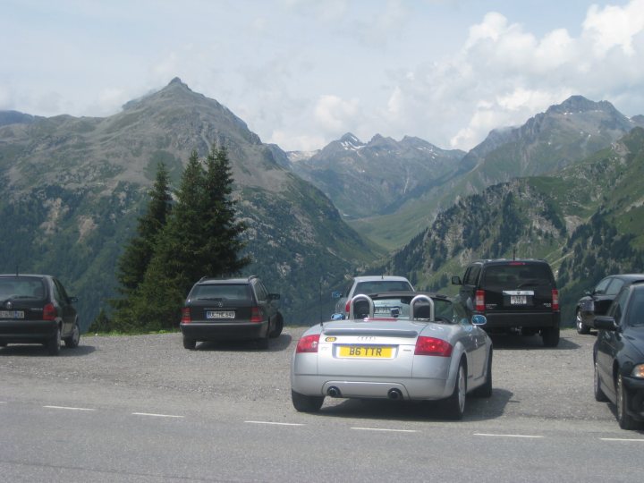 Once seen... you can't unsee it - Page 3 - The Lounge - PistonHeads UK - The image depicts a scenic outdoor setting with cars parked in a lot. The parking lot is located at the base of a mountainous area, with snow-capped mountains visible in the distance. The sky appears to be overcast, and there are no people visible in the scene.