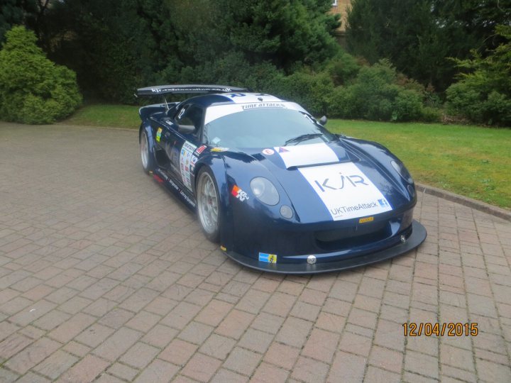 Built in Bruntingthorpe  - Page 1 - Noble - PistonHeads - The image depicts a sports car, specifically a race car, parked on what appears to be a brick driveway. It's a vibrant blue vehicle with a visible number, "KR," and some lettering, along with a small British flag on the door. A wind deflector is at the front, and there are other emblems and markings on the car that suggest it's designed for racing or is being used for performance purposes. The car is positioned on a grassy area, adjacent to a bush, and there is a date stamp at the bottom of the image, indicating it's from April 2, 2015. The overall impression is of an exciting, fast-paced environment, highlighted by the presence of this high-performance vehicle.