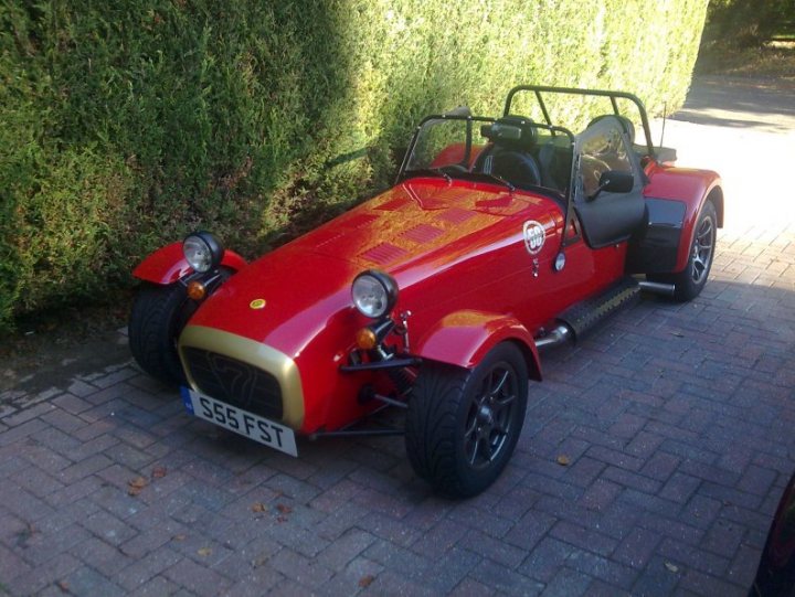 Place Pistonheads Buy - The image depicts a convertible sports car that is parked on a brick driveway. The car is primarily red, with a black canvas convertible top and a black two-seat soft top. The bodywork of the car has a slight reflection, indicating its glossy paint. This is a small-sized car with two sets of wheels in the profile, although the rims appear to be the same. The vehicle is set against the backdrop of a green hedge, adding a touch of color contrast to the red of the car. The convertible top is retracted, exposing the black interior. However, there is no visible license plate, making it challenging to provide specific details about the car.