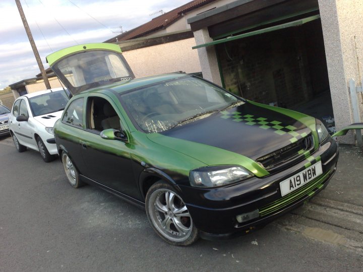 lookin for 19" alloys - Page 1 - South Wales - PistonHeads - The image displays a black car parked on a concrete surface. It is positioned in front of an open garage door. The car features a distinctive metallic green stripe on its side. The license plate on the front of the car reads "A19 WB". Another white car is visible in the background, parked farther away. The setting suggests it could be in a residential area due to the presence of a house with a visible roof.