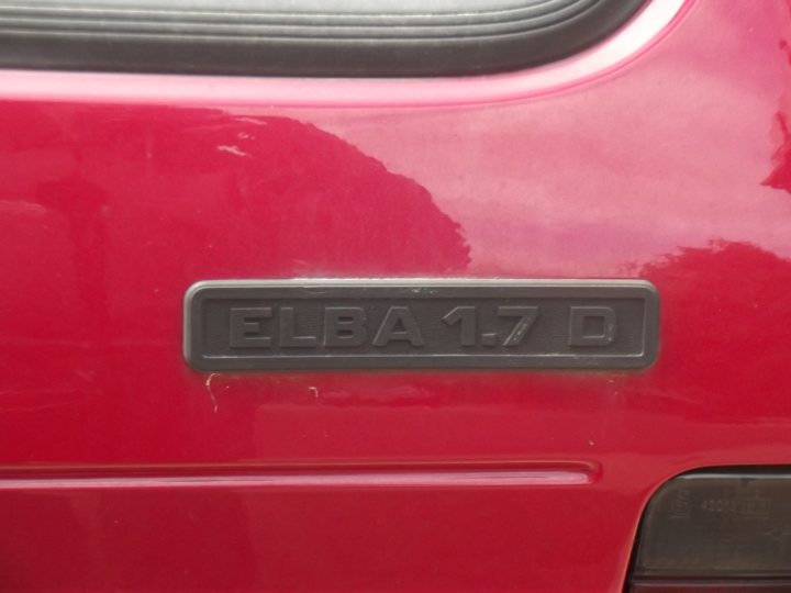 Cars you didn't know existed... - Page 249 - General Gassing - PistonHeads - The image shows a close-up view of the license plate area on the back of a red car. There is a rectangular label affixed to the car, prominently displaying the text "ELBA 17 D." The bumper is dark, contrasting with the vibrant car body. The vehicle appears to be in motion given the blurred background, indicating a photo taken during daylight with some focus on the license plate and plate holder. The style of the image is a real-world, color photograph with a shallow depth of field.