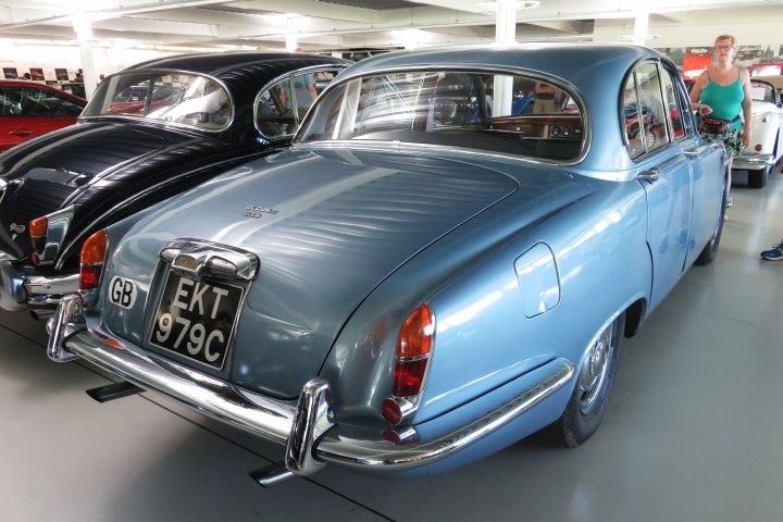 Pistonheads - The image shows a car show where two vintage cars are on display. One of the cars is a vibrant blue model parked inside a building with a white ceiling and bright lighting. The other car is an older-model black vehicle also displayed in the same setting. Both cars are stationary, suggesting that they are being showcased for visitors to admire. The cars occupy a significant portion of the image, highlighting their importance in this context.