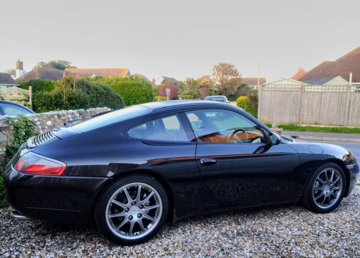 what is an 'early' 3.4 996? - Page 371 - 911/Carrera GT - PistonHeads UK - The image features a black sports car parked in front of a building. The car has a sleek design, with a sloping roofline and large alloy wheels. It appears to be a modern, high-performance vehicle, possibly an exotic or luxury model. The car is positioned at an angle to the viewer, showcasing its side profile. The background suggests an urban setting with buildings and pavement, although no people are visible in the scene.