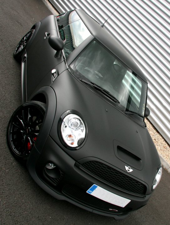 Pistonheads - The image showcases a sleek, black sports car positioned on a black surface against a backdrop of a striped building. The vehicle features prominent wheel arches and a distinctive front grille design. Notable features include a compact design, a low profile, and LED headlights. It appears to be presented in a professional manner, possibly for promotional purposes.