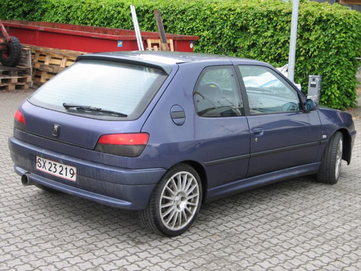 One owner FSH GTi-6 with 215K on the clock. Have I gone mad? - Page 1 - French Bred - PistonHeads - The image shows a small blue two-door hatchback parked on a brick surface. The car has a European-style license plate featuring numbers and letters. In the background, there is a pile of pallets and a patch of greenery. The vehicle appears to be in good condition with a functional side view mirror and correctly aligned wheels.