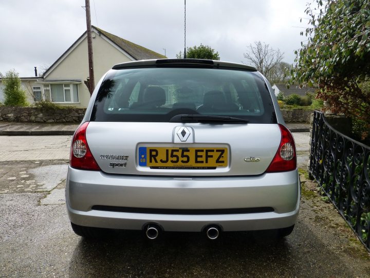 My new PH's car! - Page 1 - South West - PistonHeads - The image shows the back end of a silver-colored car parked on the side of a street. The car is compact with red tail lights. There is a license plate on the back of the car with the registration RJ55 EFZ. It's a gray day, and the car is obstructing a part of a wrought iron fence. In the background, there are houses visible.