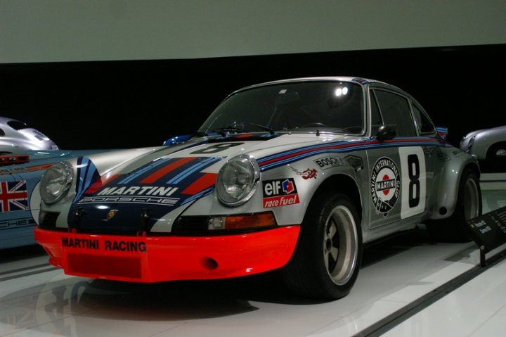 Pistonheads - The image shows a vintage racing car on display. The car is predominantly white with blue stripes and is adorned with several logos and numbers, including "8", "B", "P", and "Marino". The car has a distinct flat-12 cylinder engine. It is on a white surface, likely within a showroom or exhibition space, given the presence of another car in the background, suggesting a themed event showcasing classic cars.