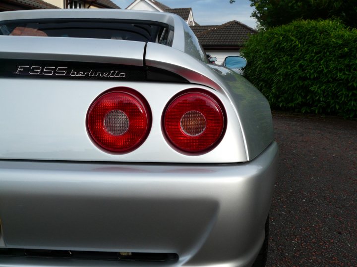 Pistonheads - The image showcases the rearview of a sports car, characterized by its sleek and shiny metallic body. It has a distinctive red taillight illuminated on both sides. The car is parked on an asphalt surface, with a hedge and a house in the background. The overall scene captures a calm and serene suburban neighborhood.