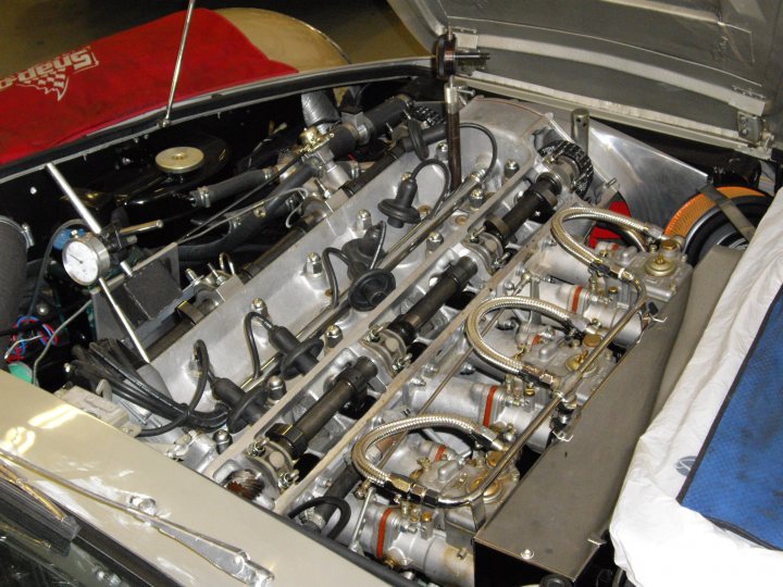 Pistonheads Superleggera - The image depicts the engine bay of a car, revealing a complex arrangement of mechanical components. A number of cylinders are visible on the right side, suggesting it is part of the engine structure. Various wires and hoses crisscross over and under the exposed engine, indicating a dense network of connections. The engine appears to be in a state of disassembly or inspection, with parts removed to expose the internal components. In the background, there's a hint of a radiator, contributing to the overall impression of the car's under-the-hood assembly.