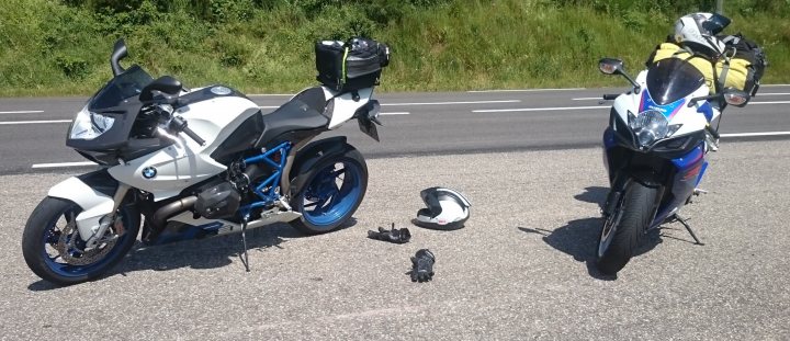 A picture a day....biker banter (Vol 4) - Page 469 - Biker Banter - PistonHeads - The image shows two motorcycles parked on a roadside. One motorcycle is closer to the foreground and appears to be white, while the other is further away and mainly covered by various items. Between the two motorcycles, there are several objects scattered about, including what seem to be gloves and a helmet, suggesting that a person may have stopped here temporarily. The road beside them indicates they are on a paved, two-lane road, with grass verges on both sides.