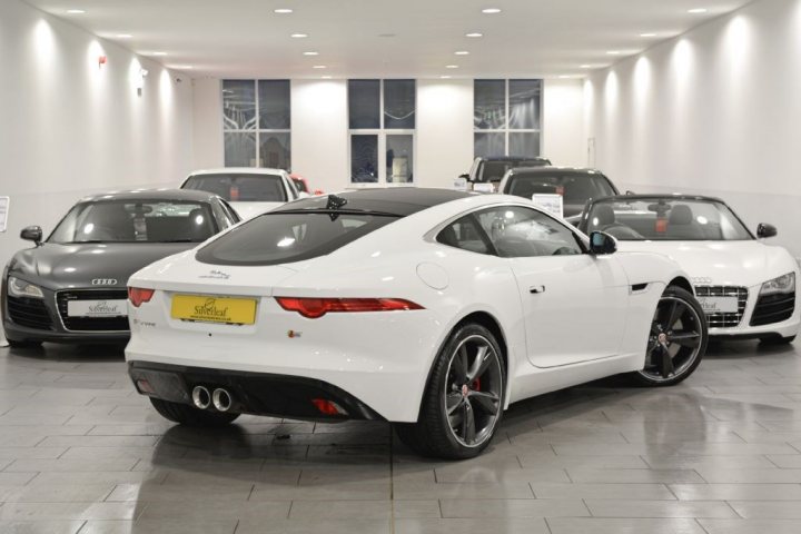 I've just bought an F-Type (pictures) - Page 1 - Jaguar - PistonHeads - The image depicts a showroom or garage setting with a group of modern sports cars on display. In the foreground, a white sports car with a distinctive lime green=colored membrane in the back and the Audi emblem is prominently visible. Two other similarly styled vehicles are parked in the background, suggesting this is a dealership or enthusiast group's collection. The cars have large rear wings, lit license plates, and black tires, suggesting a focus on performance and aesthetics. The setting has a sleek and minimalistic design, characteristic of high-end vehicle showrooms.