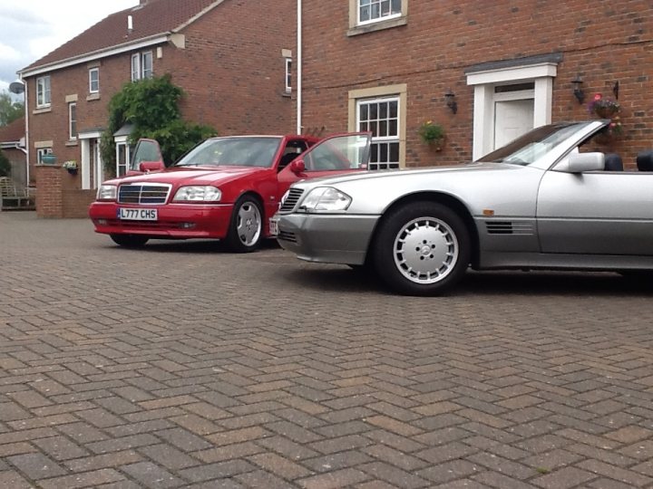 Anticipating the next rising classic stars... - Page 6 - Classic Cars and Yesterday's Heroes - PistonHeads - The image depicts a residential scene with two parked cars. A red car is parked in front of a house, and it's stylish with a glossy finish that reflects the surroundings. If we follow a line of sight from the red car through the perspective of the photographer, we would indeed see another car, a silver one, parked in the driveway. The house has a brick exterior and appears to be a typical residential house with some decorative elements like hanging baskets and outdoor lighting. The driveway is paved and provides ample space for the vehicles.