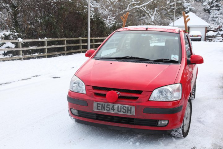 Pistonheads Open Eyes - The image captures a red car parked on a snowy road. Positioned in the middle of the frame, the car gives a clear view of its location relative to other elements in the scene. The driver's side, distinguished by its color and vibrancy, draws attention along with a particularly unique detail: a red reindeer antler is affixed to the roof, adding a festive touch to the car.

Behind the car, a fence runs along the road, with trees visible in the background, their green contrasting with the otherwise white and snow-covered environment. The landscape is blanketed in a thick layer of snow, suggesting that the photo was taken during the winter months. The absence of any other vehicles in the frame underscores the stillness of the scene. The car, with its unique antler decoration, stands out prominently against the serene winter backdrop.