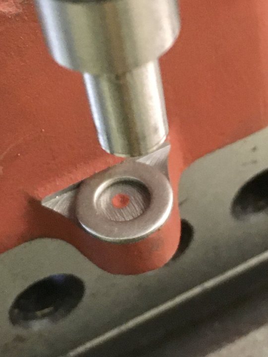 A close up of a pair of scissors - Pistonheads - The image displays a close-up view of a mechanical assembly. A red part is attached to a metallic surface with a single bolt, which appears to be in the process of being tightened. In the foreground, there's a small, cylindrical component with what seems to be an adjustable mechanism, possibly for tension or alignment. The background is out of focus but suggests an industrial setting, as indicated by the red part and the metallic surface, which could be a machine frame or a similar structure. There are no visible texts on the image.