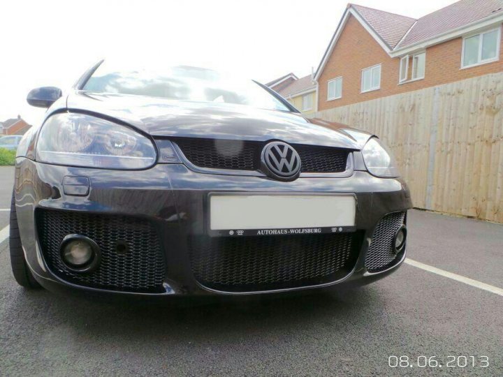 MK5 Golf - bumpers interchangeable between models? - Page 1 - Audi, VW, Seat & Skoda - PistonHeads - The image depicts a dark-colored Volkswagen car parked on an asphalt driveway in front of a brown house with a tiled pitched roof. The car is a 2012 model, as indicated by the white license plate that clearly displays the dates 08.06.2013. It's seen in the daytime, and the car features a distinctive black grille with the Volkswagen logo emblazoned in the center. The overall scene suggests a quiet suburban setting.