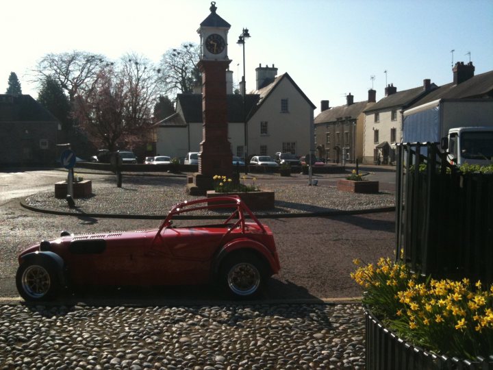 Blat Wales Pistonheads - The image captures a charming scene on a narrow cobblestone street. A classic Mini Cooper, painted in a vibrant shade of red, is parked on the right side of the street, near a lamp post. The street is flanked by residential buildings, their white walls contrasting with the asphalt of the road and the stone surface of the footpath. 

The day is clear and sunny, casting a warm glow on the scene. The sun's position suggests it might be late afternoon or early evening. On the opposite side of the street, the lush green of a tree can be seen, adding a touch of nature to the urban setting. The overall scene exudes a quaint and peaceful atmosphere, perhaps undisturbed by the hustle and bustle typically associated with city life.