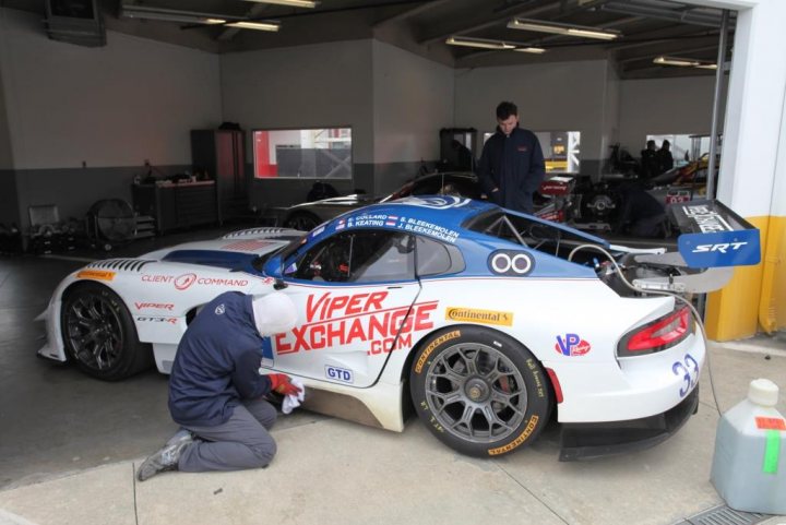 A car with a surfboard on top of it - Pistonheads - The image features a racing car parked in a garage. A technician is working on the car, kneeling on a mat in front of it, presumably performing some maintenance or repairs. The car is a blue and white Viper Racer, as indicated by the text on the side. The team that maintains the car is Constant Engineering, and there are other cars and personnel visible in the background, indicating this might be a team operation or a racing event setting.