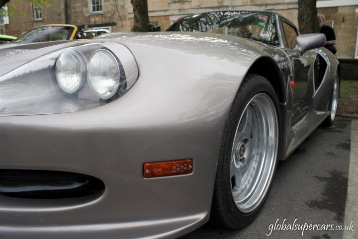 Sunday April 25th Bradford on Avon - Marocs - Page 1 - South West - PistonHeads - The image features a striking grey sports car parked on a street. The car's sleek design and clean lines reflect a modern and sophisticated aesthetic. Two large headlights look as if they are engaged in silent conversation, like alien eyes glowing against the night. The car's side is accentuated by a bold orange stripe and a chrome grill, adding a touch of luxury and elegance. As if frozen in time, the car's side profile is the star of the scene, from the smooth contours of the hood to the muscular arches of the rear wheel wells, a beautiful representation of automotive artistry.