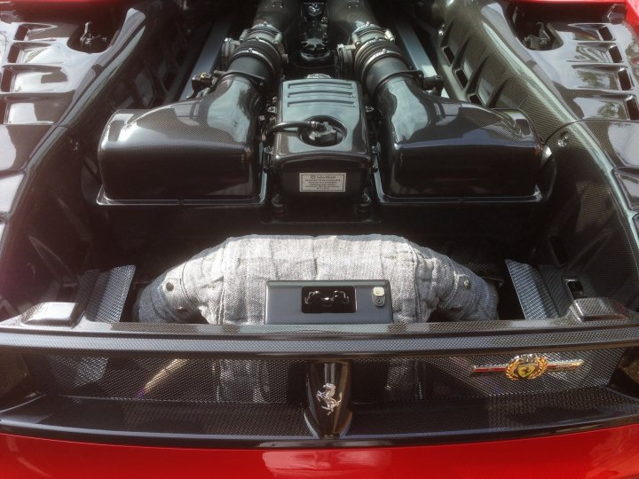 A car that is sitting in the grass - Pistonheads - The image showcases a Ferrari car's engine compartment, where the hood is open. The engine block, painted in black, stands out against the red interior of the car. Visible is a mix of mechanical components, including a large metal pipe and a radiator, both of which are essential for the car's cooling needs. In the foreground, the gas flap is open, revealing the sleek, designed metallic surface that most Ferraris are known for. This provides a glimpse of the sophisticated engineering that goes into making such a vehicle. Overall, the image showcases the intricate and powerful machinery that makes up the Ferrari car's engine and undercarriage.