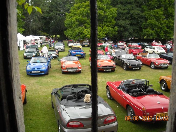 Pistonheads - The image presents a charming scene of an outdoor exhibition space filled with various vintage cars, all tightly parked into rows. Dominating the display are vibrant red and blue sports cars, their gleaming exteriors catching the viewer's eye. A few people can be seen scattered around the exhibition, adding a sense of scale to the showcase. In the foreground, a window grate adorns a gate, offering a glimpse into the world outside. The image, taken from a slightly elevated perspective, encapsulates the essence of a classic car show.