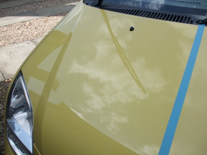 Shiney Pistonheads - The image shows a close-up view of the bonnet of a vehicle, which is painted in a glossy green color. There is a blue stripe running horizontally, parallel to the reflection of the sky. The reflection suggests that the vehicle is parked outside in daylight, possibly under a blue sky. The glossy finish indicates that the car is well-maintained and has been recently waxed or cleaned.