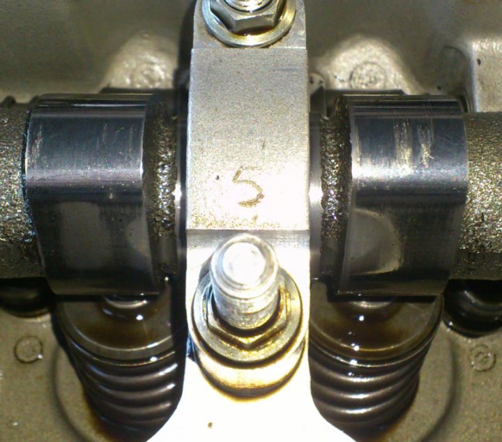 Is this camshaft done or still kind of ok?? - Page 1 - Speed Six Engine - PistonHeads - The image is a close-up view, showing a mechanical component with steel or metal parts. The central focus is on a number five indicated by an engraved or stamped measurement. This number corresponds to a specificly shaped thread typically associated with engine or mechanical components. The metallic surfaces are tarnished, and there are oil stains and residue, hinting at a mechanical or garage setting. The presence of a bold "5" in the middle of the mechanical components could indicate it's a critical number for this particular assembly.