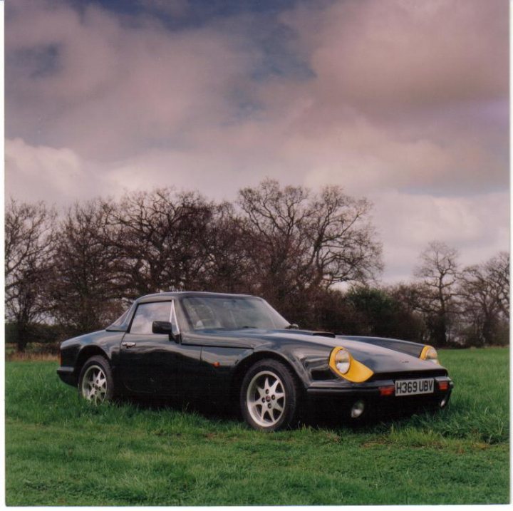 S Series hardtop - a few pics - Page 1 - S Series - PistonHeads - The image presents a striking contrast, with a dark-colored sports car parked on a vibrant green grassy field. The car is positioned in the foreground, its sleek and curved design suggesting speed and elegance. Behind the car, the backdrop is a lush, grassy expanse that stretches into the distance. This grassy field gives way to a line of dark, bare trees with no leaves, creating a dramatic contrast with the car's curvy silhouette. The overall effect is one of tranquillity and bold statement, with the car as the focal point against a serene and natural setting.