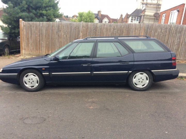 Classic (old, retro) cars for sale £0-5k vol 2 - Page 19 - General Gassing - PistonHeads - The image depicts a **blue station wagon parked at the side of a street**. The car is adjacent to a wooden fence and is also situated close to a house with a chimney visible. The scene suggests a somewhat residential or suburban area, with the vehicle appearing to be in good condition.