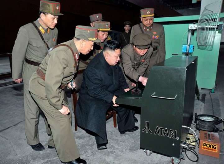 North Korea photoshop contest - Page 11 - The Lounge - PistonHeads - The image shows a group of men dressed in formal military uniforms, who are gathered around an arcade video game, possibly a table-topping unit, given the wooden table and seating arrangement visible. They appear to be engrossed in playing the game or inspecting the device. The men exhibit a range of expressions, suggesting interest and engagement. The setting is indoors, and the style of the image indicates it might be from a time when such gaming units were not widely accessible to the public.